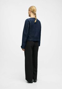 Dunkelblaue Denimjacke mit einem cropped Design, sichtbaren Nähten und geradem Saum, kombiniert mit weit geschnittenen schwarzen Hosen und klobigen schwarzen Schuhen.