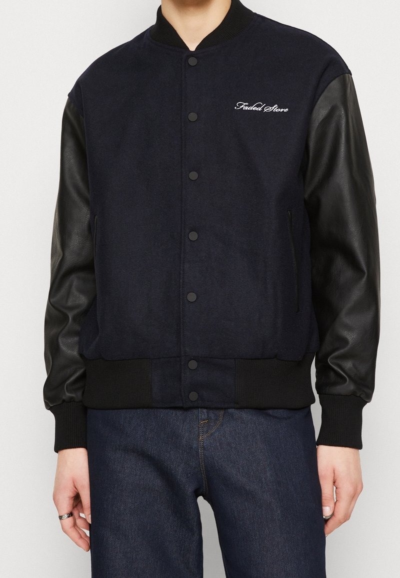 Giacca varsity blu navy con maniche in pelle nera, chiusura con bottoni, polsini a costine e ricamo "Faded Store" sul petto.
