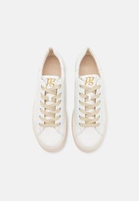 Baskets blanches en cuir avec une surface texturée, lacets beiges et un petit logo doré sur la languette. Bout arrondi et design minimaliste.