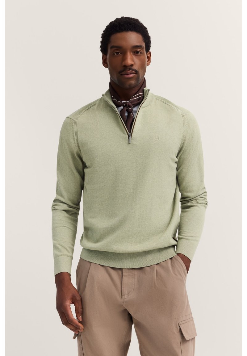 Maglione verde chiaro con collo a mezza zip, polsini e orlo a coste; abbinato a pantaloni cargo beige. Texture liscia, minimo dettaglio del logo.