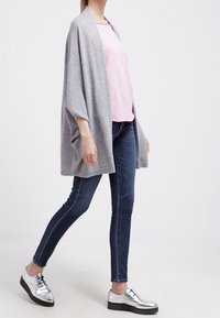 Grå stickad sjal bärs över en rosa skjorta, tillsammans med mörkblå skinny jeans och silverfärgade snörskor. Enkel design och avslappnad passform.