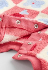 Koralvliesstoff mit einem gemusterten Design, das rote und blaue Formen zeigt. Enthält Druckknöpfe entlang des Kragens sowie ein weiches, strukturiertes Futter.