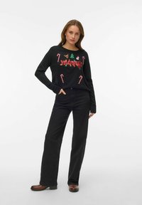 Juodas megztinis su šventiniais siuvinėjimais, tarp kurių medelis, Kalėdų senelis, saldainių lazdelių atvaizdai ir raudonais bei žaliais siūlais išsiuvinėtas žodis „Merry“. Dėvimas su juodais džinsais.