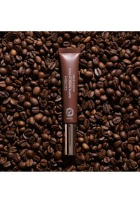 Rör med GOSH soft'n tinted lip balm med SPF15 placerad på en bakgrund av rostade kaffebönor.