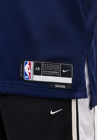 Maillot NBA Swingman bleu foncé avec étiquette taille 48 et logo Nike au-dessus d’un short noir avec un swoosh blanc et une bande latérale.
