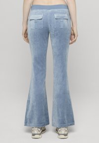 Pantaloni evazați din velur albastru deschis cu textură fină, având două buzunare spate cu închidere cu capse și o talie lată.