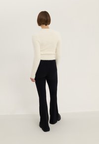 Un pull blanc et duveteux à manches longues associé à un pantalon évasé noir côtelé. L'ensemble présente une coupe ajustée avec des surfaces texturées.