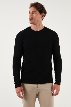 Schwarzes langärmeliges Rippenshirt mit Rundhalsausschnitt, das ein tailliertes Design und strukturierten Stoff aufweist, kombiniert mit hellbeigen Hosen.