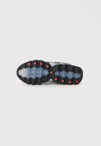 Semelle de basket en caoutchouc noir avec un design ondulé, sections translucides, accents rouges vifs et grips texturés circulaires pour l'adhérence.