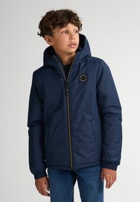 Marineblaue isolierte Jacke mit Reißverschluss vorne, elastischen Bündchen und Kapuze. Verfügt über ein rundes Logo-Patch auf der linken Brust.