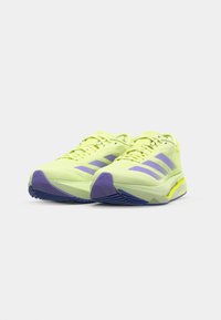 Scarpe sportive verde lime con accenti viola e design a tre strisce. Parte superiore in mesh traspirante, suola ammortizzata e suola in gomma testurizzata.