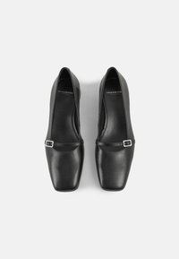 Ballerines en cuir noir avec un bout carré, dotées d'une fine lanière verticale ornée d'une boucle métallique sur le dessus. Finition lisse, design minimaliste.