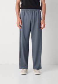 Pantalones de hombre con cintura elástica en suave tela gris, con un corte holgado y acentos de abertura lateral, combinados con zapatillas de colores claros.