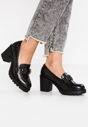 Zwarte leren hakken met een chunky hak, voorzien van een decoratieve gesp en een gestructureerde zool. Draag ze met vergrijsde denim met rafels.