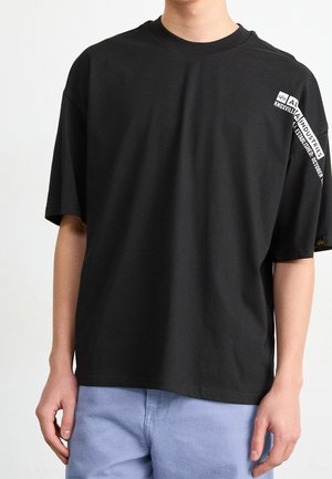 Czarny bawełniany T-shirt o luźnym kroju, z krótkimi rękawami i nadrukowanym tekstem na prawym ramieniu. Prosty design, bez widocznych wzorów ani akcentów.