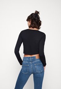 Czarna krótka bluzka z długim rękawem w połączeniu z niebieskimi dżinsami z wysokim stanem. Dżinsy mają dwie tylne kieszenie i małą skórzaną metkę.