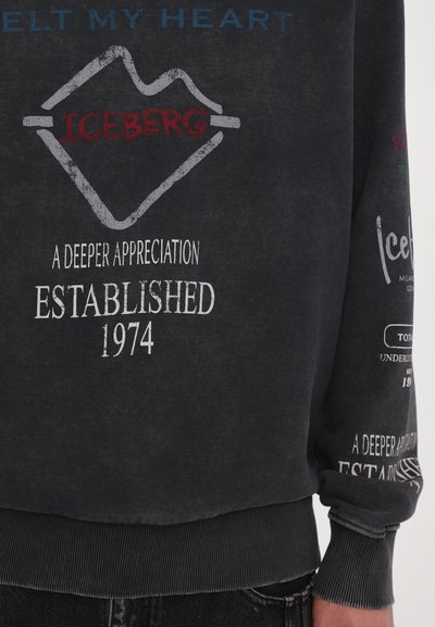 Sweatshirt noir avec un texte imprimé, incluant "ICEBERG" en rouge et "Established 1974" en blanc. Doté d'un col rond et de poignets côtelés.