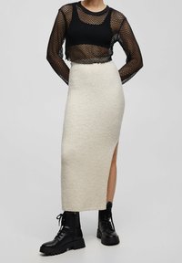 Haut noir en maille à manches longues avec une coupe cropped, associé à une jupe en tricot crème mi-longue avec une fente sur le côté, et des bottes de combat noires chunky.