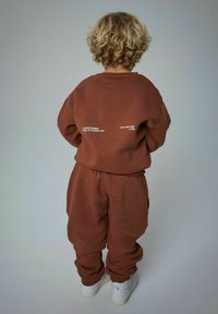 Brun sweatshirt og sweatpants sæt lavet af blødt stof. Bagfra ses hvide tekstdetaljer på bagsiden af toppen, elastisk taljebånd og manchetter.