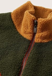 Fleecejakke med høj krave, lynlås og farveblokke i grøn og sennepsgul med en blød, tekstureret overflade.