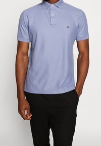 Ljuspurplett polo skjorta i mjukt tyg, med en treknapplåsning och en liten logotyp på bröstet, matchad med svarta byxor.