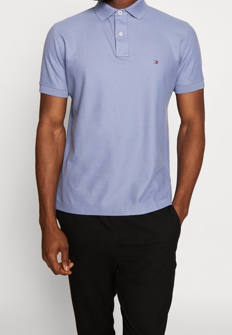 Ljuspurplett polo skjorta i mjukt tyg, med en treknapplåsning och en liten logotyp på bröstet, matchad med svarta byxor.