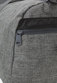 Mochila de tela gris con una superficie texturizada, que cuenta con un bolsillo con cremallera y un tirador gris etiquetado como "BORG" para un acceso fácil.