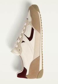 Baskets beiges en cuir et daim. Accents blancs, bout arrondi et semelle brune texturée avec un motif en zigzag.