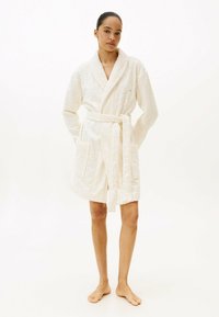 Accappatoio corto bianco con motivi circolari in rilievo, colletto a scialle, due tasche frontali e cintura abbinata annodata in vita.