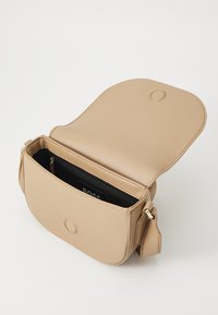 Borsa a tracolla in pelle beige con pattina arrotondata, superficie testurizzata e tasca interna con zip. Presenta un dettaglio del logo circolare e una tracolla regolabile.