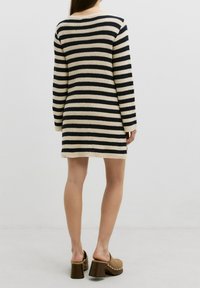 Robe tricotée rayée en crème et marine, avec des manches longues et un col rond. Associée à des mules à talons bruns avec des accents cloutés.