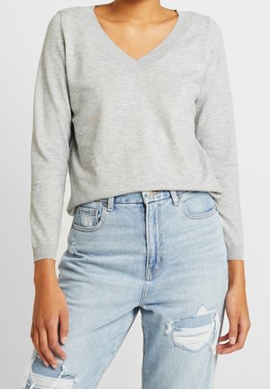 Grauer Pullover mit langen Ärmeln und V-Ausschnitt, aus weichem Material gefertigt. Kombiniert mit hellblauen, hochgeschnittenen Jeans mit Used-Effekten.