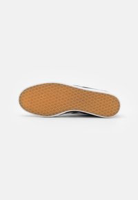 Tênis preto com sola de borracha texturizada em padrão de favo de mel. Detalhes brancos ao redor da sola e um design superior liso.