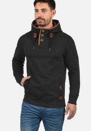 Sudadera negra de algodón, con capucha forrada en marrón, tapeta de cuatro botones, cordones ajustables y un bolsillo lateral con detalle.