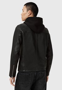 Veste en cuir noir avec un design zippé et une capuche noire. Comprend des manches longues et des zips sur les poignets.