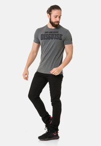 Grauer kurzärmeliger T-Shirt mit dem Text "CIPO AND BAXX DISGUISE". Kombiniert mit schwarzen Slim-Fit-Hosen und schwarzen Sneakers mit pinken Akzenten.