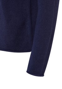 Dunkelblauer gestrickter Pulloverärmel und unterer Torso-Bereich mit sichtbarer Textur und einem sauberen Saum vor einem weißen Hintergrund.