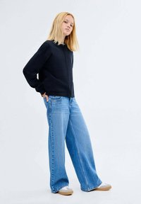 Črn zip-up pulover, široke svetlo modre jeans hlače, svetlo rjave čevlje za enostavno obuvanje. gladka tkanina, sproščen kroj in brez vidnih vzorcev.