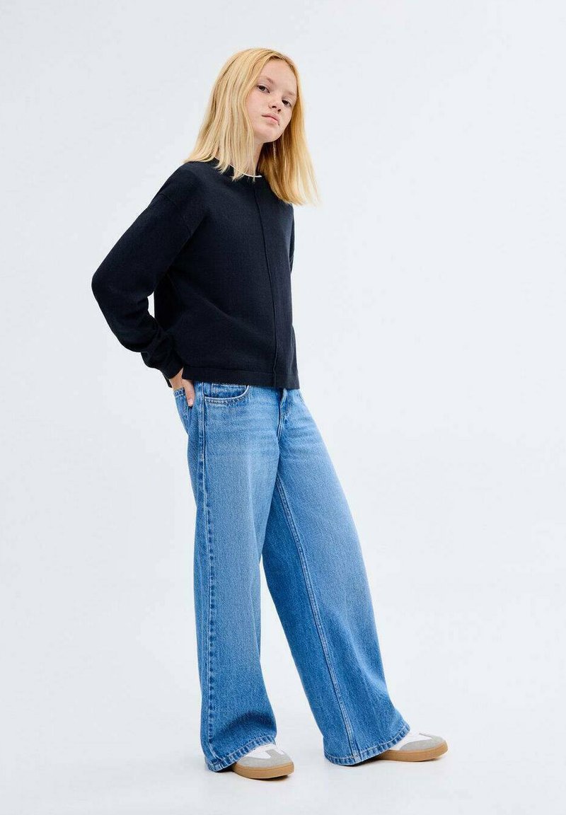 Črn zip-up pulover, široke svetlo modre jeans hlače, svetlo rjave čevlje za enostavno obuvanje. gladka tkanina, sproščen kroj in brez vidnih vzorcev.