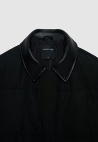 Black puffer jacket with a sleek leather collar. Features quilted texture and a tag labeled “CALLIOPE,” size S. Simple, modern design.