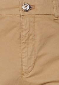 Shorts en coton beige clair avec une texture lisse, dotés d'une poche avant, d'une fermeture à bouton en métal et de détails de couture subtils.