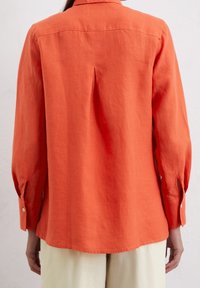 Orange linnejacka med knäppning och långa ärmar, med en ok och en veck baktill, avslutad med manschettknappar.
