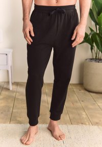 Pantaloni de trening negri realizați dintr-un material moale, prevăzuți cu talie elastică cu șnur și manșete conice la glezne.