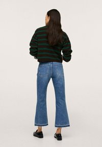 Pull court rayé vert et noir associé à un jean évasé bleu clair taille haute avec un ourlet brut. Une paire de chaussures noires complète la tenue.