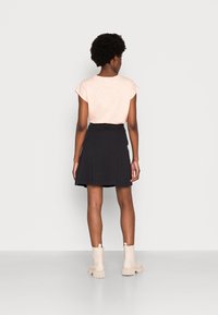 Top de manga corta rosa pálido combinado con una falda negra acampanada, llevado con botas de tobillo beige; texturas suaves y diseño casual.