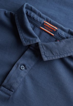 Ciemnoniebieska koszulka polo z teksturowanej tkaniny. Wyposażona w klasyczny kołnierzyk, zapięcie na dwa guziki i metkę marki w kolorze czerwonym i pomarańczowym.