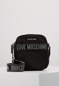 Černá nylonová crossbody taška ve tvaru obdélníku, s prostornými přihrádkami a popruhem s textem "LOVE MOSCHINO" tkaným šedou barvou.