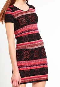 Robe tricotée avec un col rond, des manches courtes et une silhouette ajustée, ornée d'un motif géométrique dans des teintes de noir, rose et rouge.