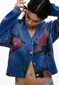 Blauer, gerippter Cardigan mit strukturierten Blumenmustern in Rosa und Grün. Verfügt über einen V-Ausschnitt, Knopfverschluss und eine kurze Passform.