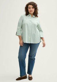 Camicia button-up a righe verde chiaro con maniche a tre quarti abbinata a jeans blu a gamba dritta e ballerine in suede marroni.